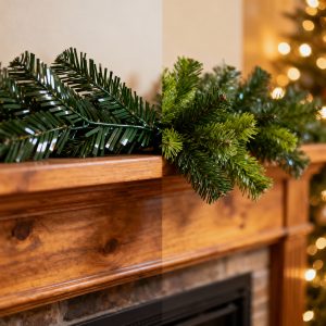 Close-up of a fireplace mantel with plastic artificial Christmas garland on one side and fresh and realistic faux greenery on the other, decorated with warm holiday lights.